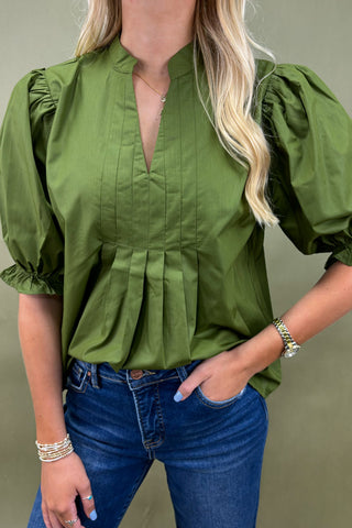 Person wearing a green blouse with puffed sleeves and blue jeans against a plain background