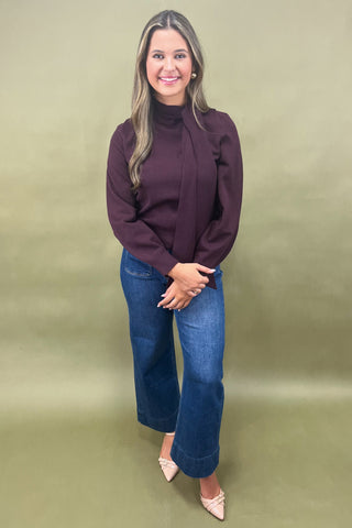 Woman wearing a dark purple sweater and blue jeans against a green background