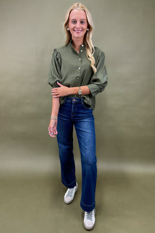Woman wearing a green shirt and blue jeans against a plain background
