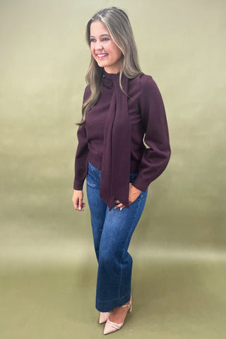 Woman wearing a purple blouse and blue jeans against a beige background