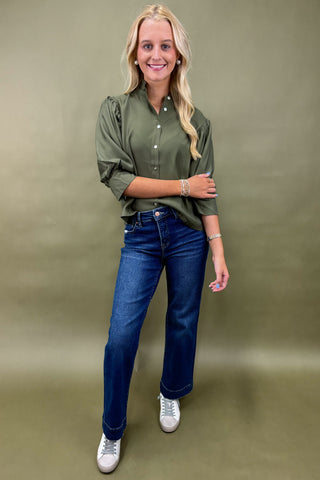 Woman wearing a green shirt and blue jeans against a green background