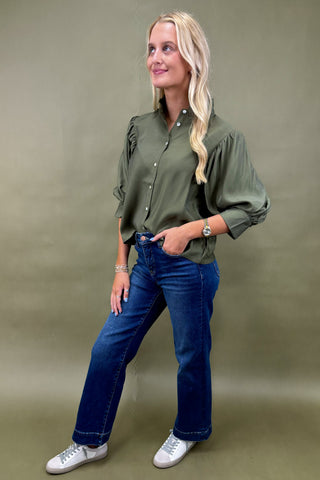 Woman wearing an olive green shirt and blue jeans against a beige background