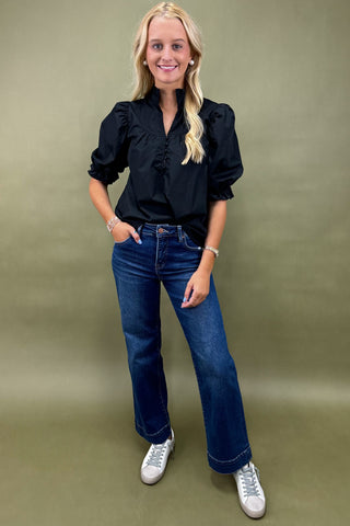 Woman wearing a black blouse, blue jeans, and white sneakers on a green background