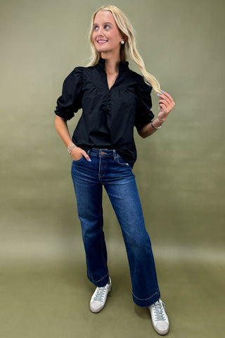 Woman wearing a black blouse, blue jeans, and white sneakers on a green background