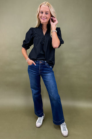 Woman wearing a black blouse and blue jeans against a green background