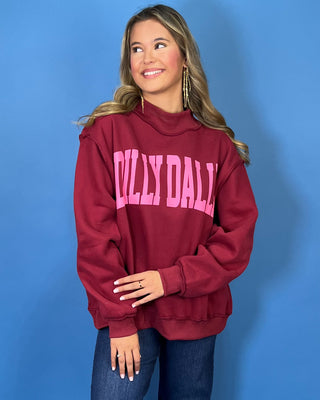 Burgundy Dilly Dally graphic sweatshirt with bold pink lettering, mock neckline, long sleeves, ribbed trim, and a relaxed oversized fit.