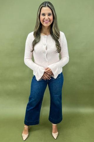 Woman wearing a white blouse and blue jeans against a green background