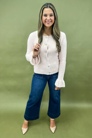 Woman wearing a white cardigan and blue jeans against a green background