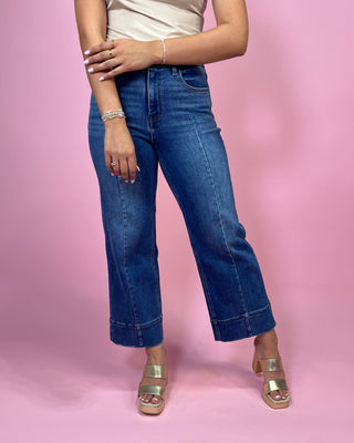 Person wearing blue jeans and gold sandals on a pink background