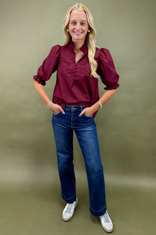 Woman wearing a burgundy blouse and blue jeans against a green background