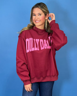 Burgundy Dilly Dally graphic sweatshirt with bold pink lettering, mock neckline, long sleeves, ribbed trim, and a relaxed oversized fit.