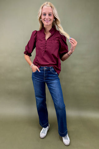 Woman wearing a burgundy blouse and blue jeans against a green background