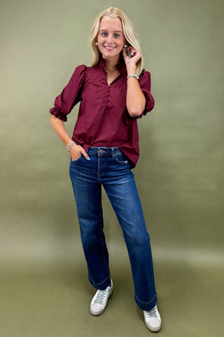 Woman wearing a burgundy blouse and blue jeans against a green background