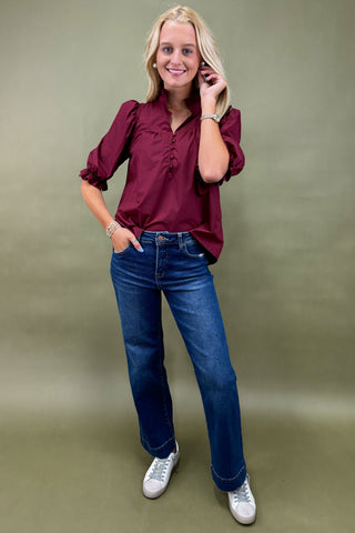 Woman wearing a burgundy blouse and blue jeans against a green background