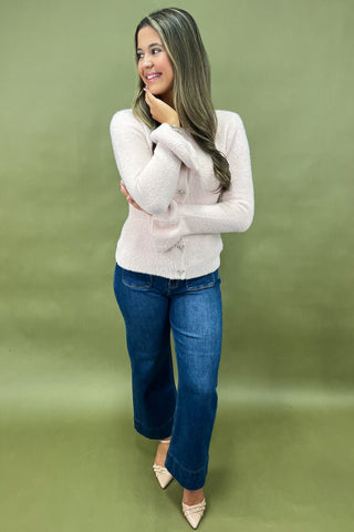 Woman wearing a light gray sweater and blue jeans against a green background
