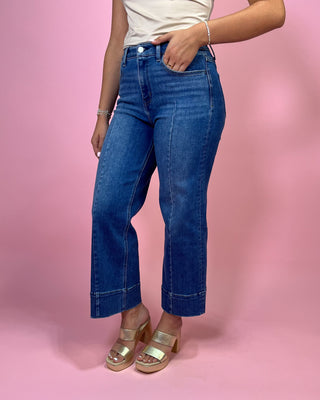 Person wearing blue jeans and gold sandals on a pink background
