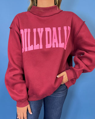 Burgundy Dilly Dally graphic sweatshirt with bold pink lettering, mock neckline, long sleeves, ribbed trim, and a relaxed oversized fit.
