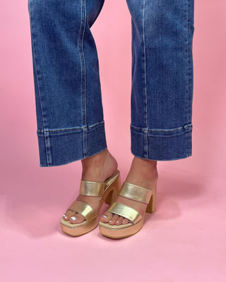 Gold platform sandals worn with blue jeans on a pink background