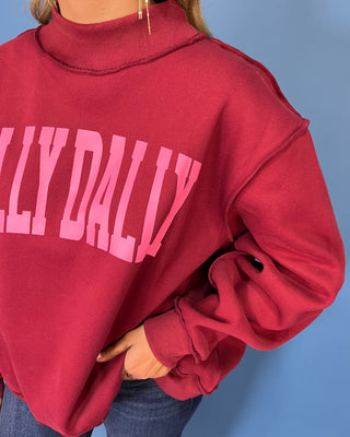 Burgundy Dilly Dally graphic sweatshirt with bold pink lettering, mock neckline, long sleeves, ribbed trim, and a relaxed oversized fit.