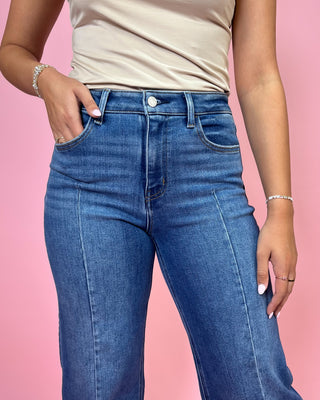 Person wearing blue jeans and a beige top against a pink background