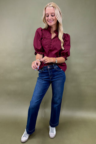 Woman wearing a burgundy blouse and blue jeans against a green background