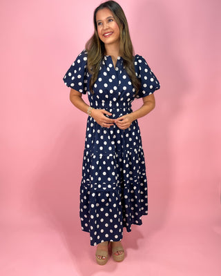 Woman wearing a navy blue dress with white polka dots on a pink background