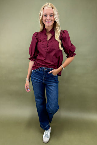 Woman wearing a burgundy blouse and blue jeans against a green background