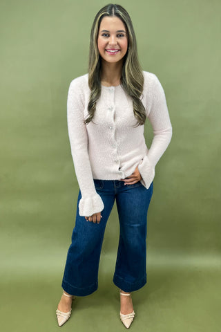 Woman wearing a white cardigan and blue jeans on a green background