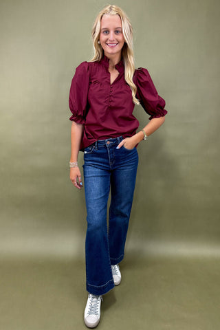 Woman wearing a burgundy blouse and blue jeans against a green background