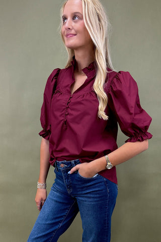 Woman wearing a burgundy blouse with puffed sleeves and blue jeans against a green background