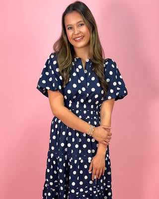 Woman wearing a navy blue dress with white polka dots against a pink background