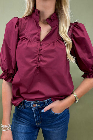 Woman wearing a burgundy blouse with puffed sleeves and blue jeans against a green background