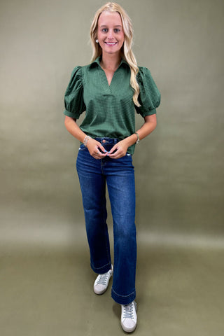 Woman wearing a green blouse and blue jeans against a plain background