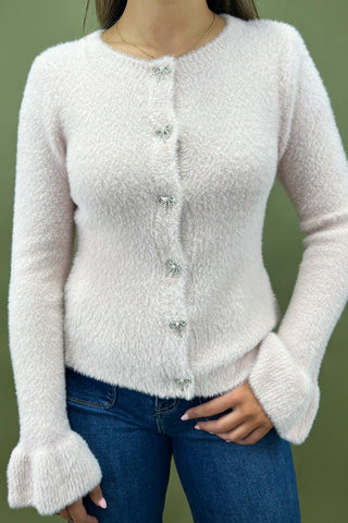 Person wearing a white textured cardigan with blue jeans on a green background