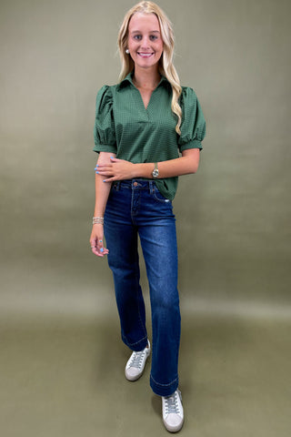 Woman wearing a green checkered blouse and blue jeans on a beige background
