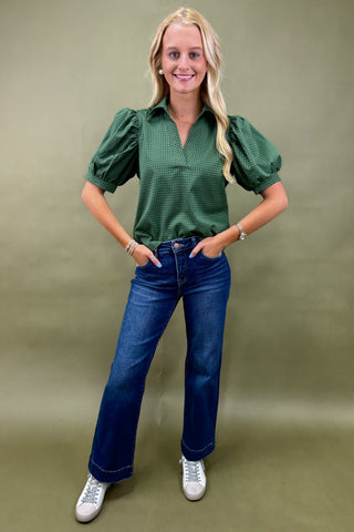 Woman wearing a green patterned blouse and blue jeans against a green background