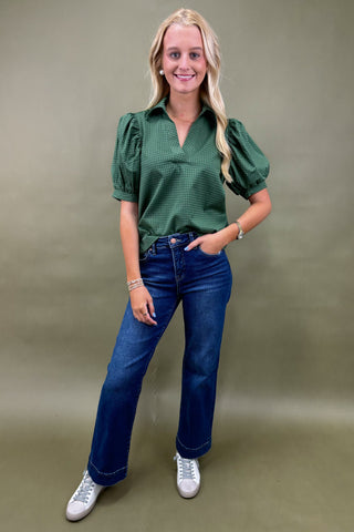 Woman wearing a green blouse and blue jeans against a plain background