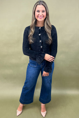 Woman wearing a black cardigan and blue jeans against a green background