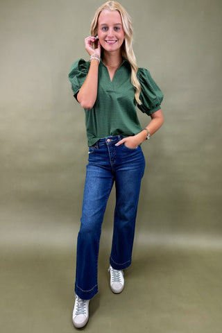 Woman wearing a green blouse and blue jeans against a beige background