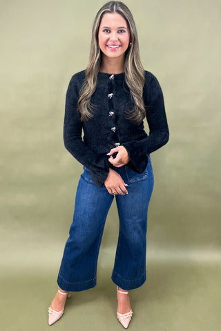 Woman wearing a black cardigan and blue jeans against a green background