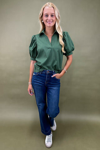 Woman wearing a green blouse and blue jeans against a green background