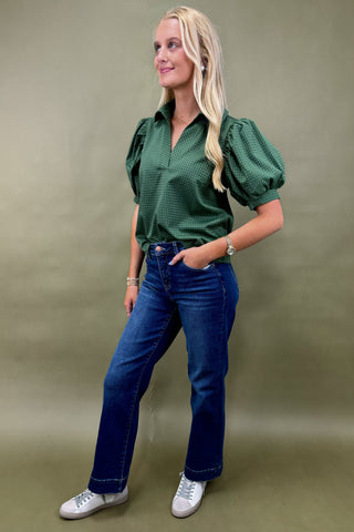 Woman wearing a green patterned blouse and blue jeans on a beige background