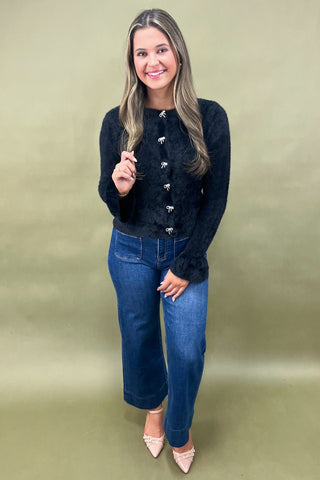 Woman wearing a black cardigan and blue jeans against a green background