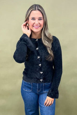 Woman wearing a black sweater with white buttons and blue jeans against a beige background
