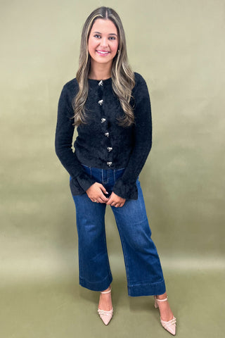 Woman wearing a black cardigan and blue jeans against a green background