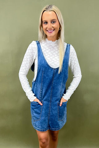 Woman wearing a denim dress over a white long-sleeve shirt against a green background