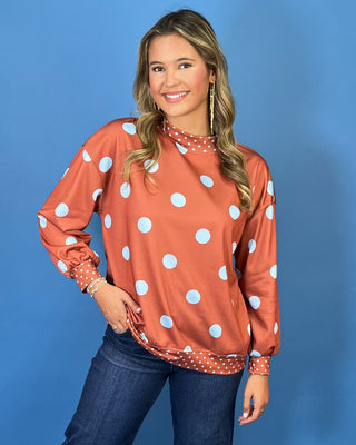 Rust polka dot long sleeve top with oversized light blue dots, contrasting mini dot mock neckline, cuffs and hem, and a relaxed fit.