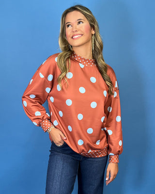 Rust polka dot long sleeve top with oversized light blue dots, contrasting mini dot mock neckline, cuffs and hem, and a relaxed fit.