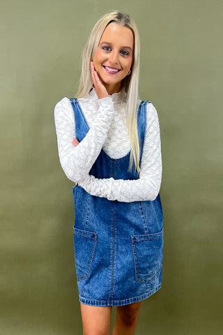 Woman wearing a denim dress over a white sweater against a green background