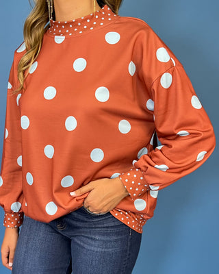 Rust polka dot long sleeve top with oversized light blue dots, contrasting mini dot mock neckline, cuffs and hem, and a relaxed fit.